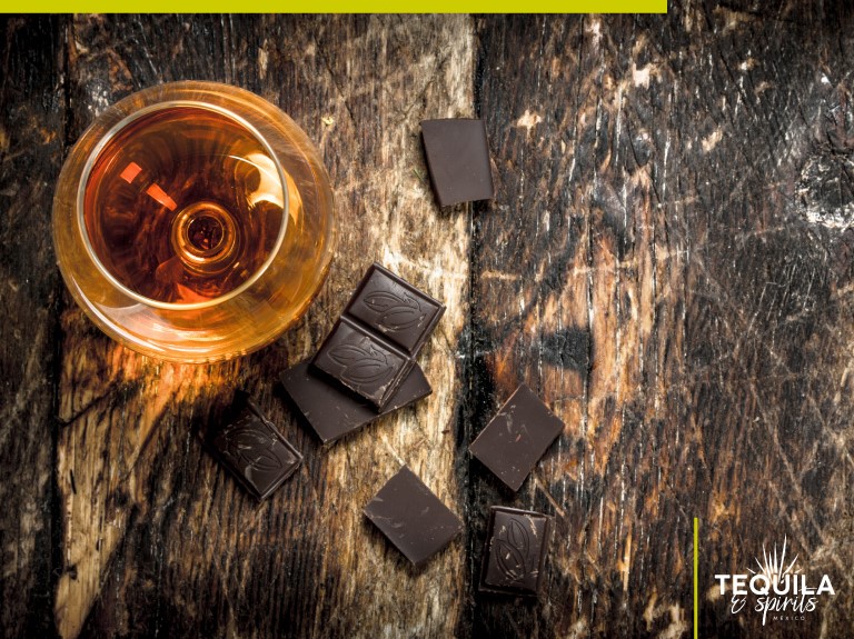 A glass of chocolate-infused tequila with pieces of chocolate bar around.