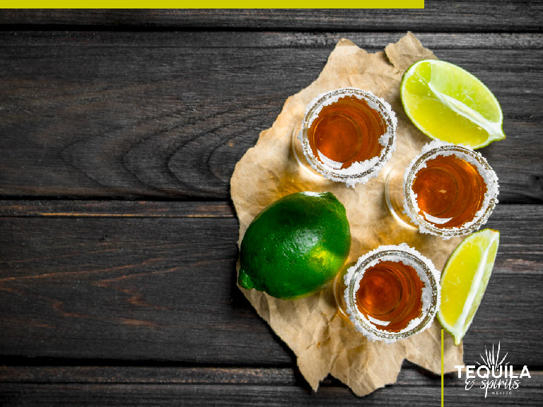 Three shots of añejo tequila with lemon slides besides them.